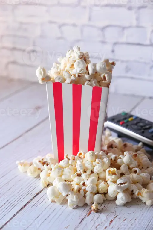 Popcorn dan remote control di sofa, siap untuk menonton film